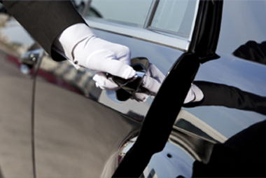A hand of a person wearing white gloves about to open the car door