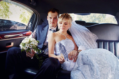 A bride and groom sitting in the back of a car holding flowers